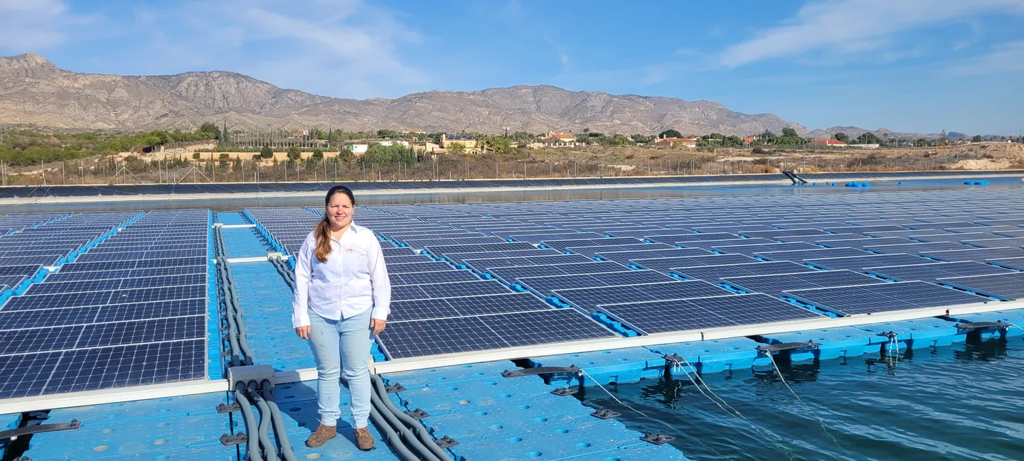 Paneles fotovoltaicos montados sobre flotadores en una balsa de agua, vistos desde una pasarela con una persona en primer plano.