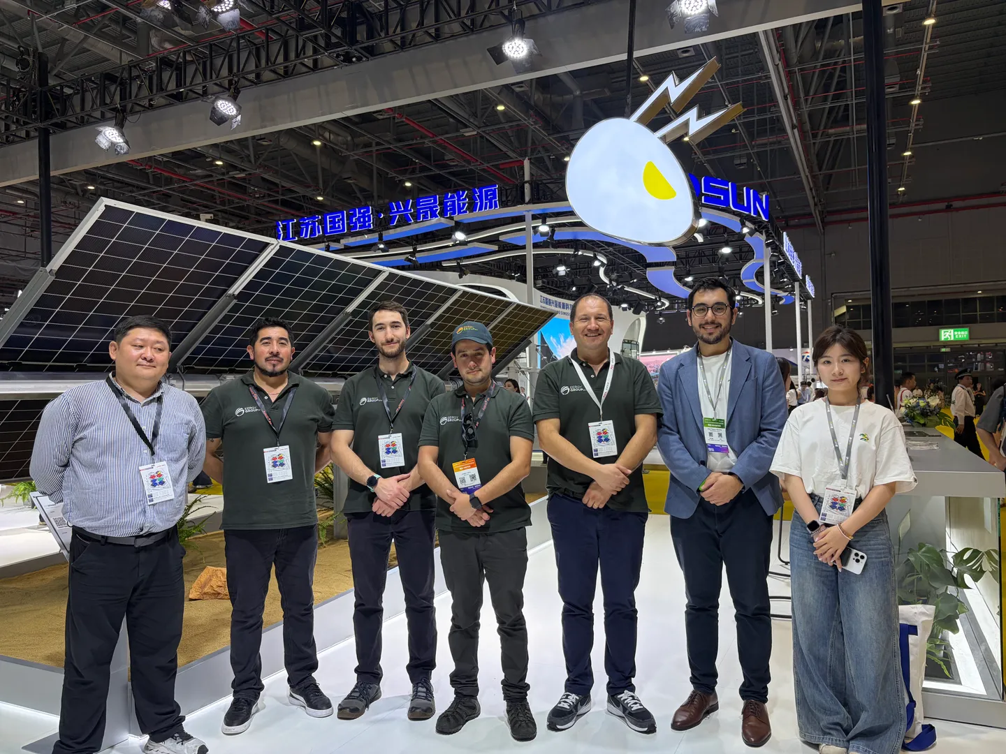 Siete personas posan frente a un stand de tecnología solar; cuatro llevan polera de EERGYGROUP.