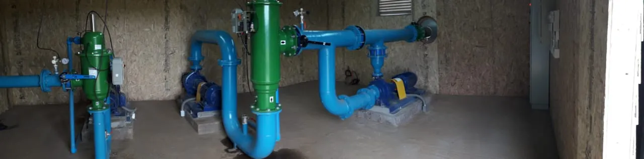 Caseta con bombas centrífugas horizontales, dos filtros verticales verdes y cañerías azules con válvulas.